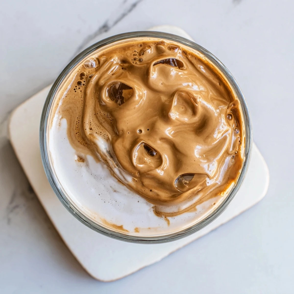 Golden-brown Whipped Dalgona Coffee topping swirls into rich milk, served in a glass with a rustic wooden backdrop.  