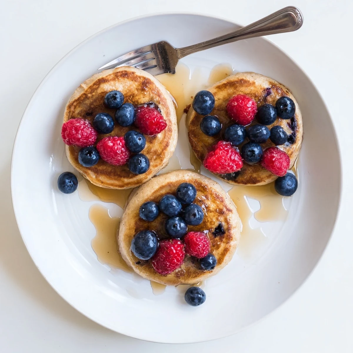Golden brown banana pancakes stacked on a plate, topped with fresh berries and a drizzle of maple syrup.  