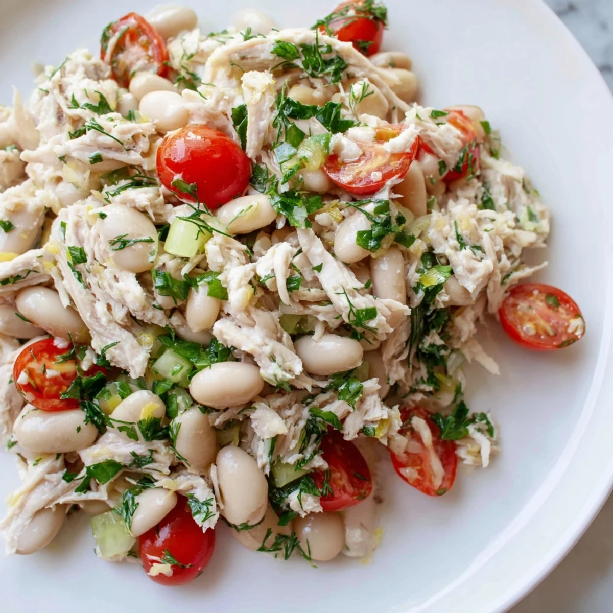 Close-up of Lemony White Bean Chicken Salad showcasing shredded chicken, cannellini beans, and diced red onion with a glossy lemon dressing.