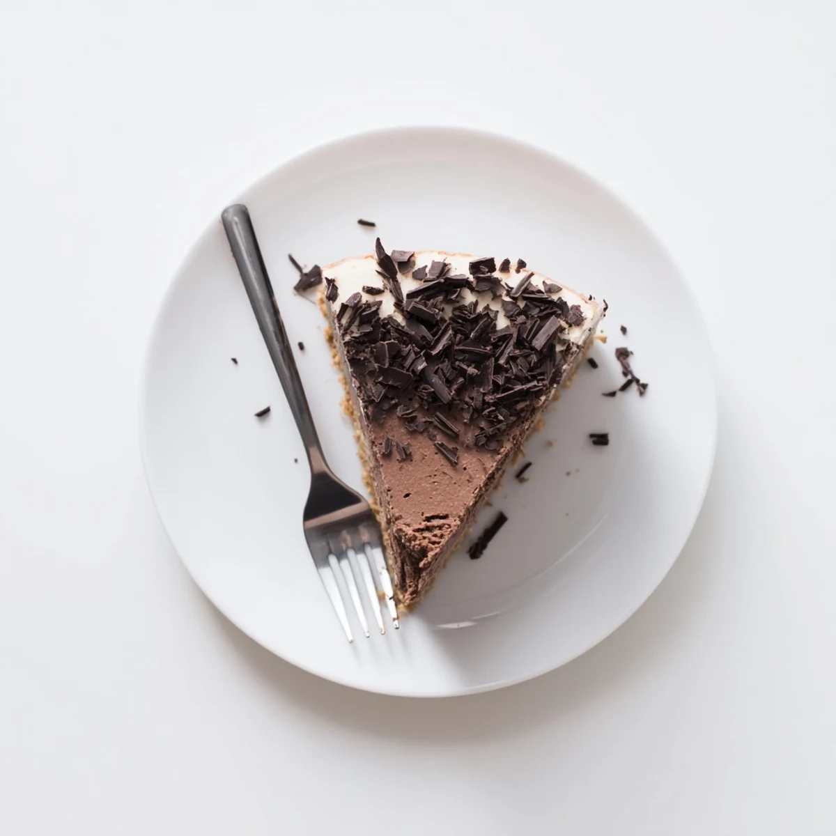 A slice of rich, dark chocolate Lighter Chocolate Cottage Cheese Cheesecake topped with fresh raspberries and chocolate shavings on a white plate.  