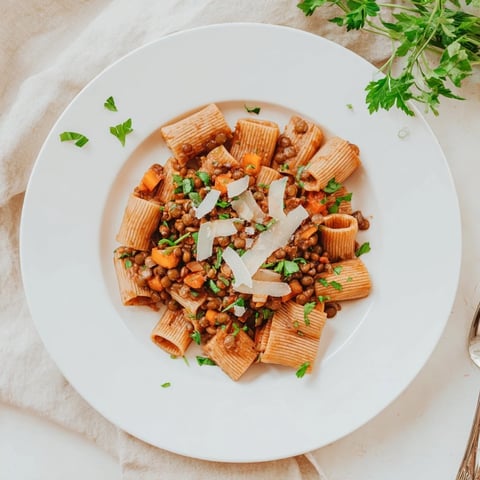 Steaming bowl of High-Fiber Lentil Bolognese, a hearty pasta dish with vibrant holiday garnishes.