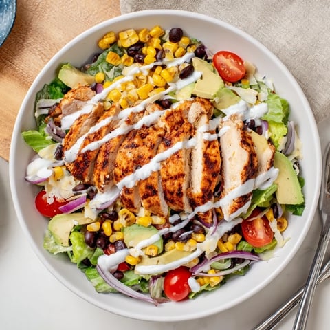 Grilled BBQ chicken slices atop crisp romaine with corn, black beans, tomatoes, and creamy ranch drizzle in this vibrant salad.