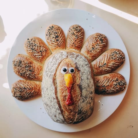 Crisp, artisan turkey-shaped sourdough bread with rustic scoring, shown on a wooden board, perfect for Thanksgiving gatherings.