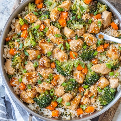 Golden seared chicken pieces and bright green broccoli florets rest atop fluffy white rice in a skillet, drizzled with a glossy honey garlic sauce in this One Pan Honey Garlic Chicken Broccoli Rice recipe.