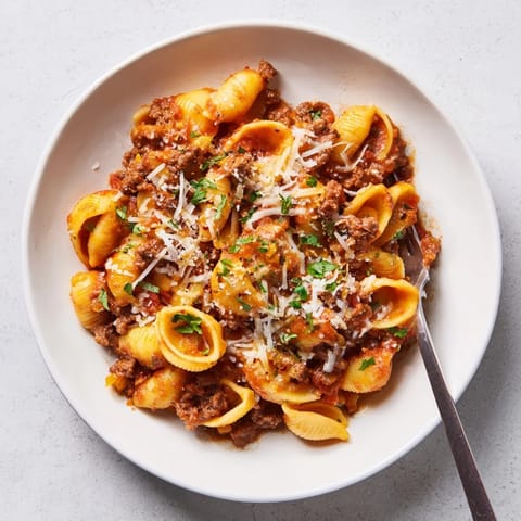 Spoon serving of One Pot Creamy Beef and Shells, revealing creamy red sauce melting over cheddar and pasta shells in a rustic pot.