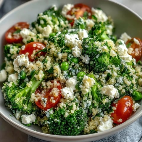 A colorful grain bowl with quinoa, steamed broccoli, sweet peas, and tangy feta crumbles, dressed in lemon vinaigrette for a fresh vegetarian meal.