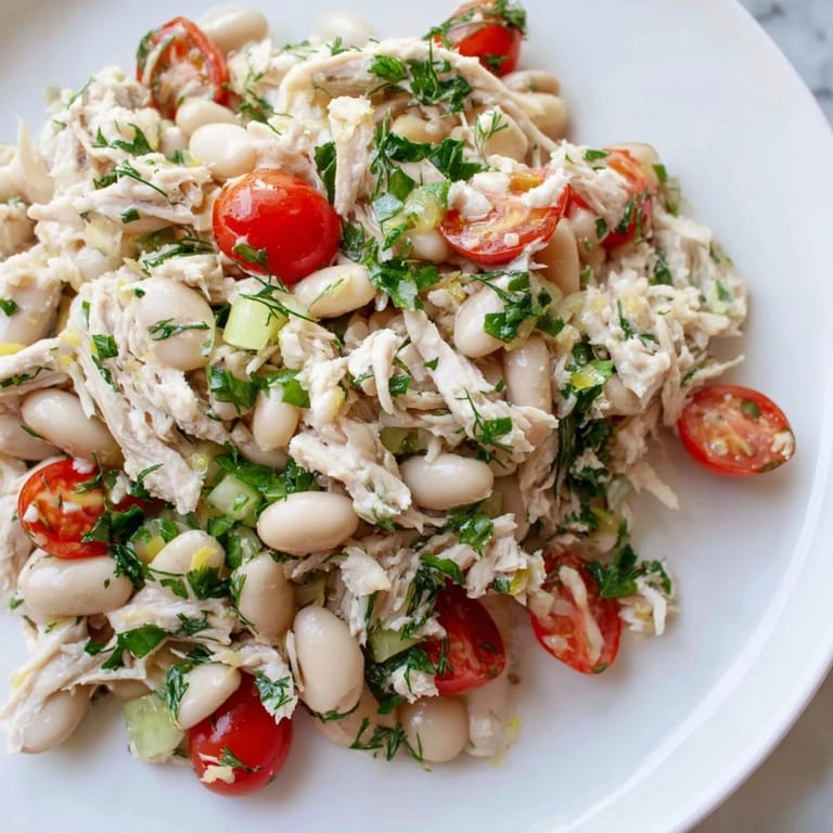 Close-up of Lemony White Bean Chicken Salad showcasing shredded chicken, cannellini beans, and diced red onion with a glossy lemon dressing.