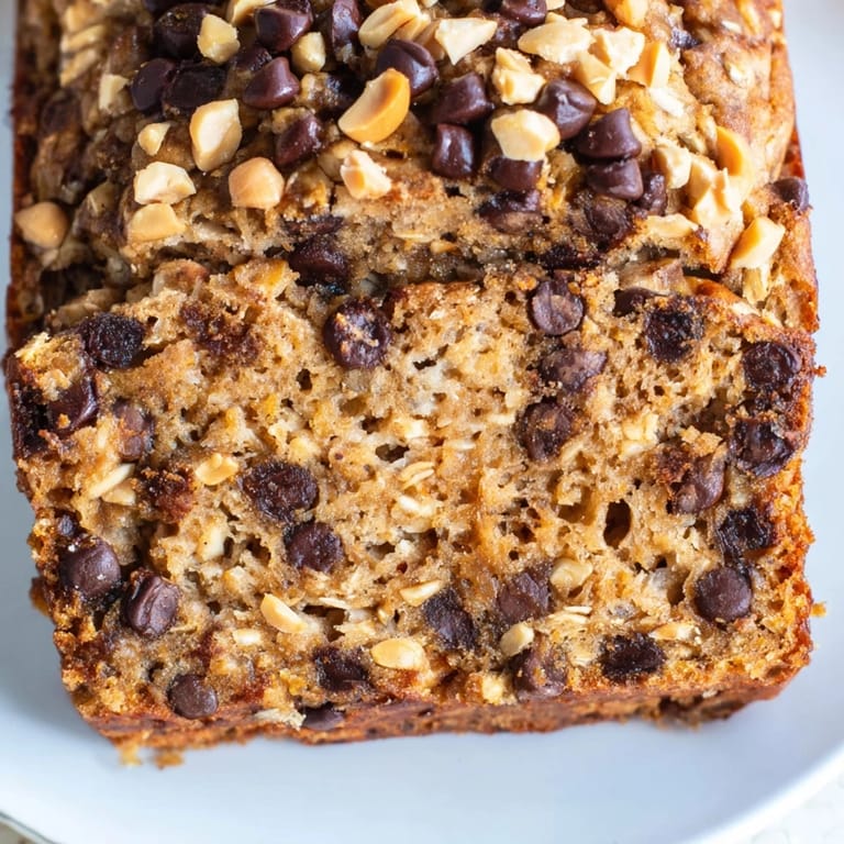 Freshly baked loaf of Chocolate Chip Peanut Butter Oatmeal Banana Bread cooling on a wire rack, revealing a golden-brown crust and hearty oat texture inside.  