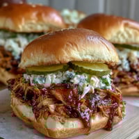Mouthwatering BBQ pulled chicken sliders on soft buns, topped with tangy coleslaw for a flavorful party bite.