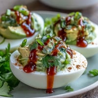 Creamy avocado deviled eggs with spicy Sriracha drizzle make a colorful, crowd-pleasing appetizer.